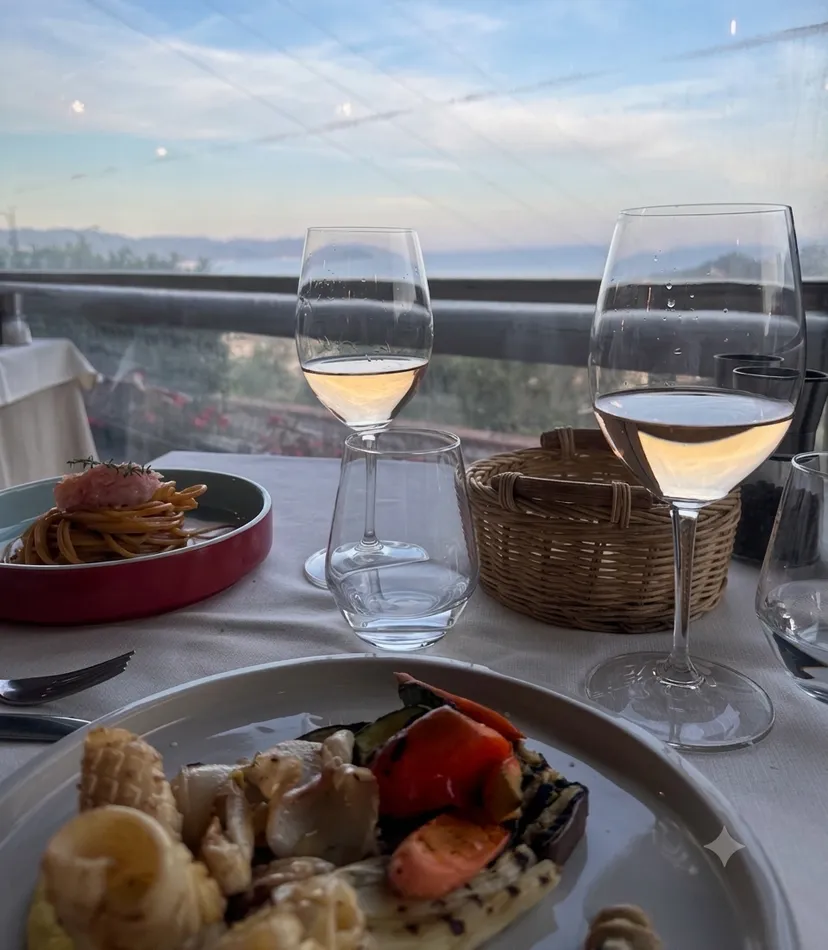 Spaghettis et légumes grillés sur une table de la terrasse, avec deux verres de vin blanc